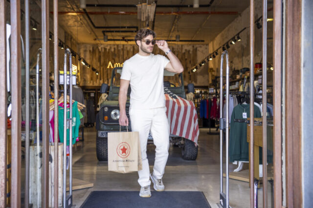 Man walking out of fashion retail store with shopping bag during commercial lifestyle video shoot in Greece